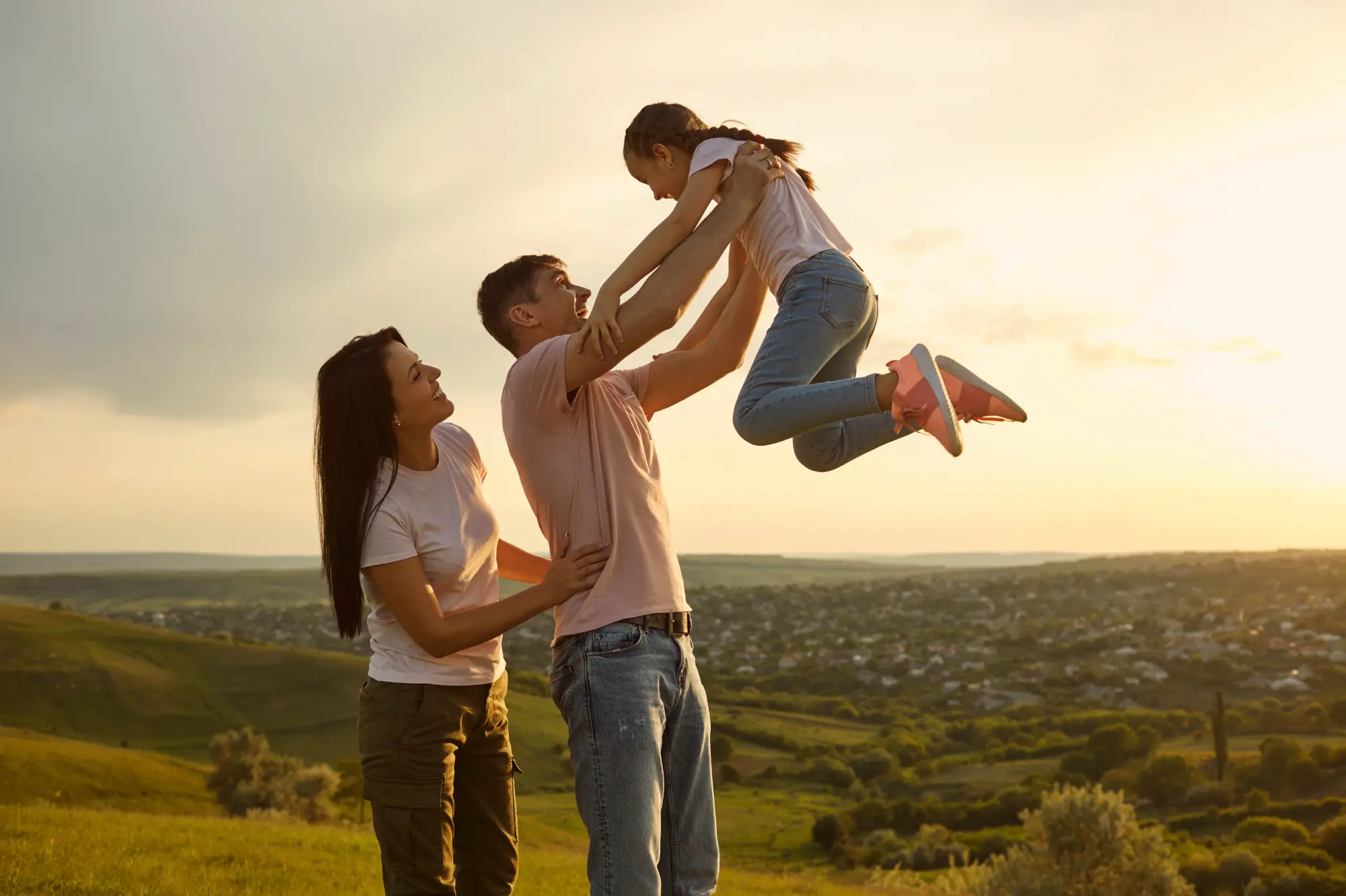 Joyful young family having fun with their daughter in mountains at sunset